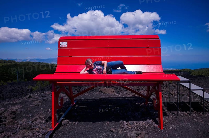 Elderly woman lying on huge red bench