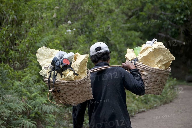 Local man carrying sulphur blocks and gas mask in baskets down from volcano crater