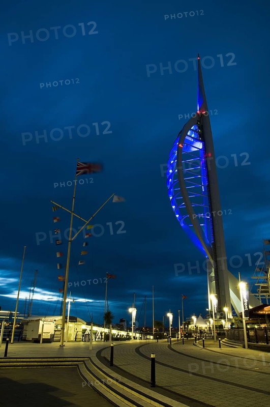 View of waterfront with Spinnaker Tower illuminated under stormclouds at dusk
