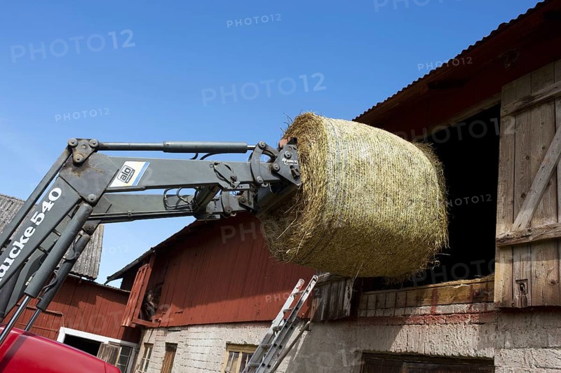 Loading round bale of hay into hayloft with front loader bale spike on Case tractor