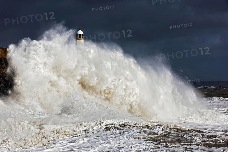 Coastal town seafront and lighthouse bombarded by waves in storm