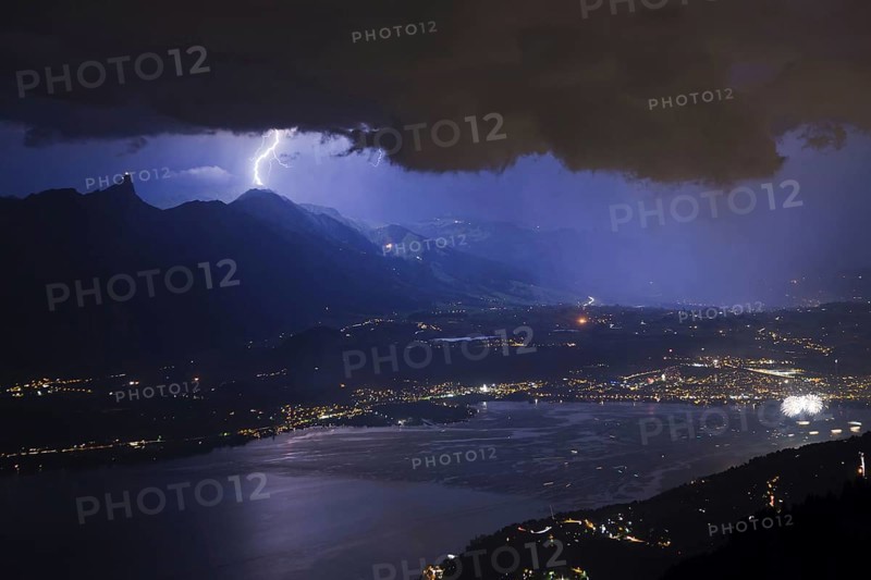 Thunderstorm with lightning and fireworks over town and lake at night