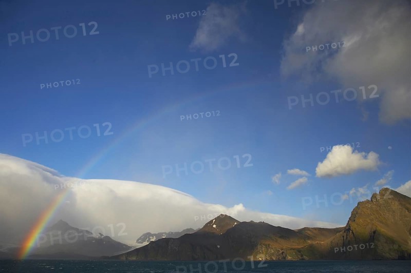 View of rainbow and moon over the coastline