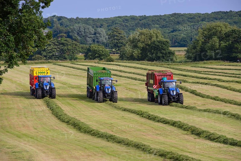Three tractors with feed wagons picking up cut grass