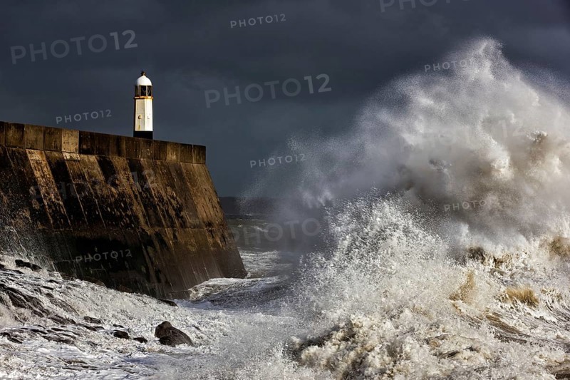 Coastal town seafront and lighthouse bombarded by waves in storm