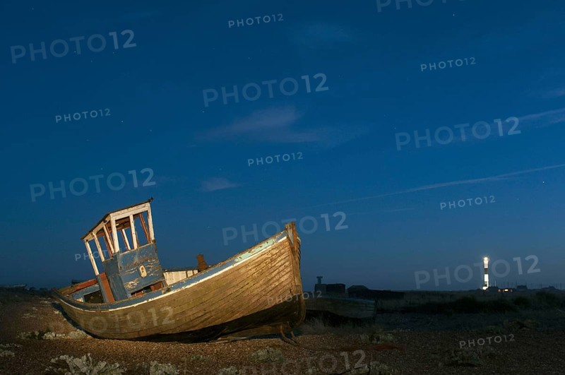Abandoned fishing boat on shingle beach illuminated by torchlight at night