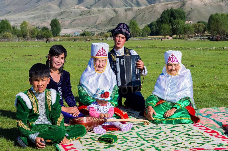 Kazakh family in traditional dress listening to the music of an accordion player