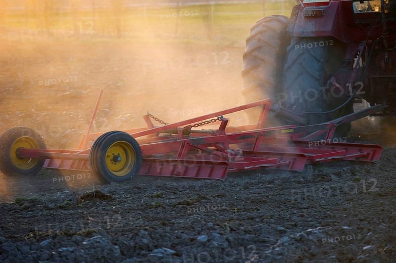 Close-up of Vaderstad cultivator cultivating a field planting bed in a dusty field at sunset