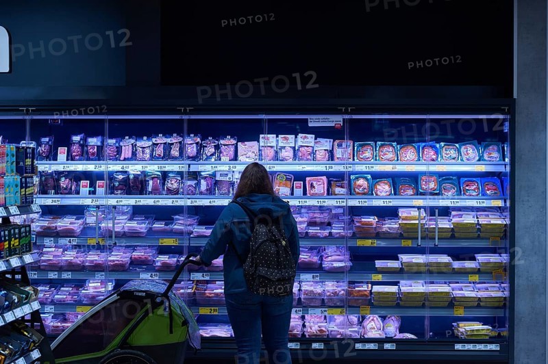 A woman with a pram is standing in front of the meat and sausage cooling shelf