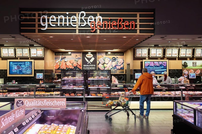 Man in orange jacket and shopping trolley standing in front of the service counter for cheese