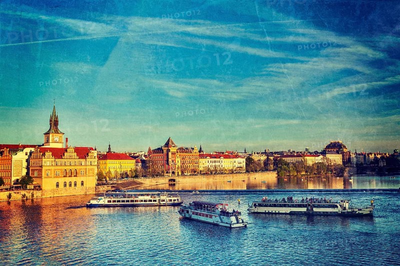 Vintage retro hipster style travel image of Vltava river with tourist boats and Prague Stare Mesto embankment view from Charles bridge on sunset with grunge texture overlaid. Prague