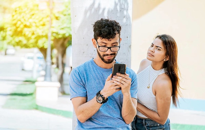 Suspicious girl spying on her boyfriend phone. Jealous girl spying on her boyfriend's cell phone in the park