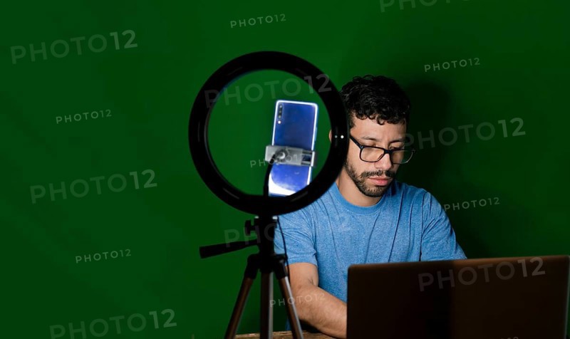 Guy with laptop making video blog on phone. Man giving classes in a video call. Online classes concept. Man giving online classes with phone. Guy on a video call working from home
