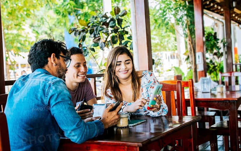 Young friends in a coffee shop with their cell phones having a good time. Three people in a coffee shop with phones having a good time. Three teenage friends on their cell phones in a coffee shop