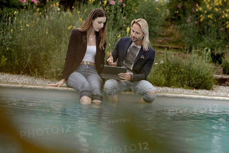 Man and woman with laptop sitting by the poolside