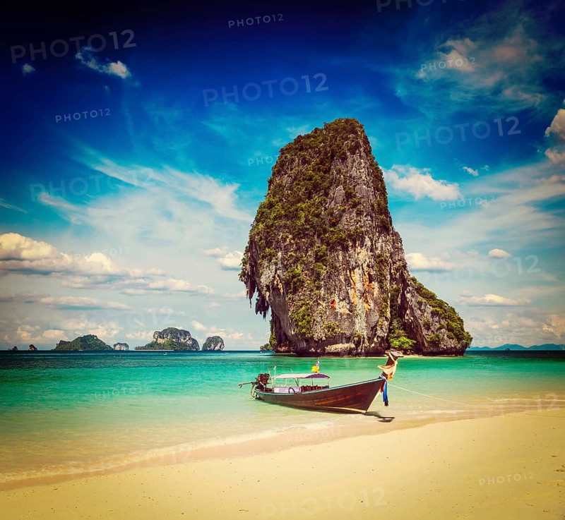 Vintage retro effect filtered hipster style travel image of long tail boat on tropical beach with limestone rock
