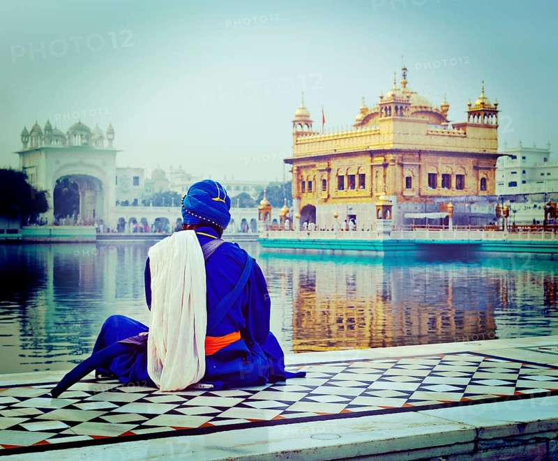 Vintage retro hipster style travel image of unidentifiable Seekh Nihang warrior meditating at Sikh temple Harmandir Sahib. Amritsar