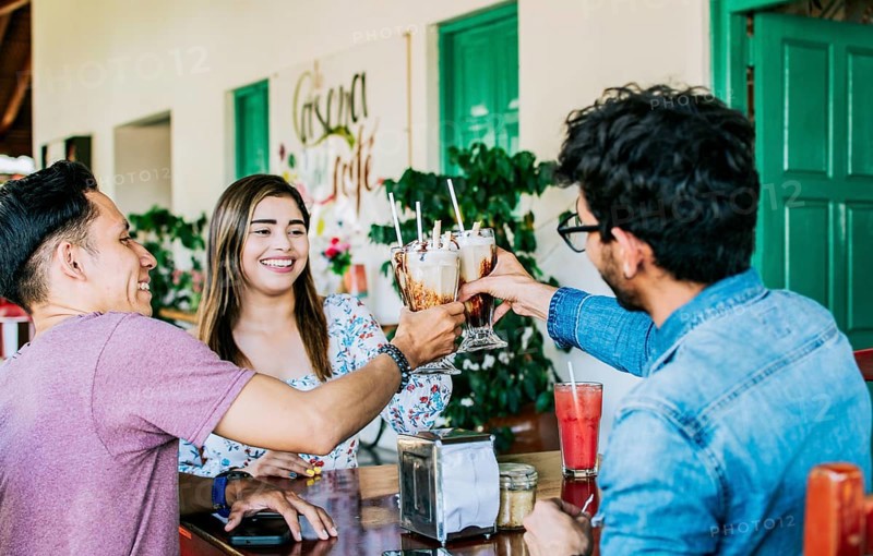 Happy friends enjoying a milkshake in a coffee shop. Three happy best friends meeting and toasting in a coffee shop