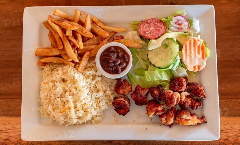 Plate of breaded shrimp with rice and salad on the wooden table. Top view of breaded shrimp with french fries and salad served on wooden table. Seafood food concept served on the table