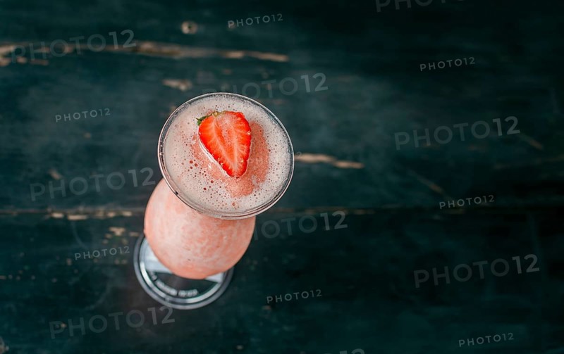 View of strawberry milkshake on dark wood. View from above of delicious strawberry smoothie with a strawberry on top on wood. Top view of strawberry smoothie on dark wooden table