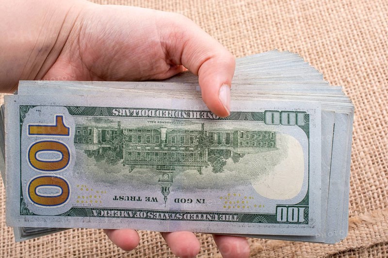 Hand holding banknote bundle of US dollar on a linen canvas background