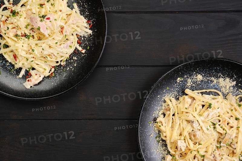 Top view of two plate with pasta with ham and mushrooms