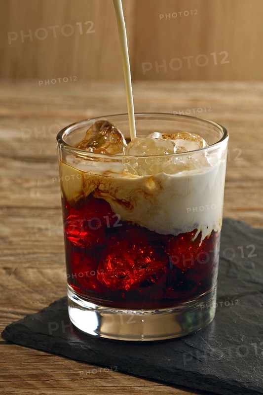 Pouring cream into cocktail White Russian. Vodka