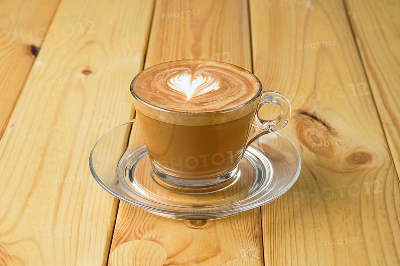 Cappuccino in transparent glass cup on wooden table