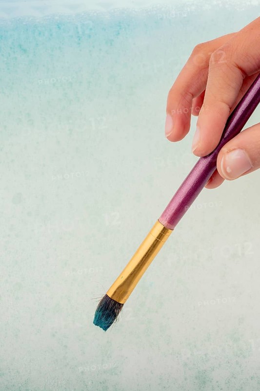 Hand holding a paint brush on water covered with foam