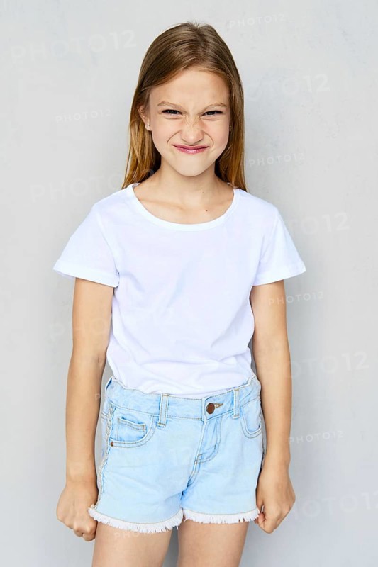 Young angry and mischievous girl in white t-shirt and jeans shorts posing in studio