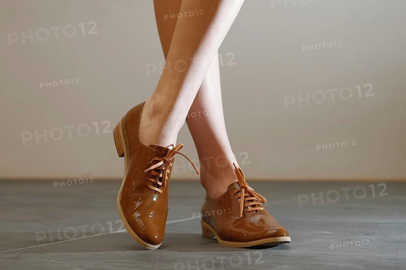 Cropped image of bare female legs in patent leather shoes with shoelaces