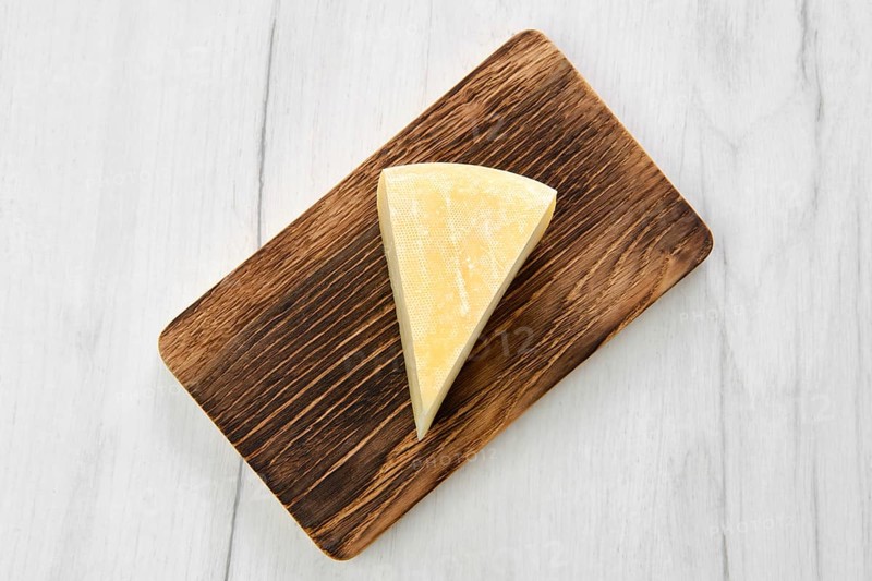 Top view of triangular piece of goat cheese on wooden cutting board