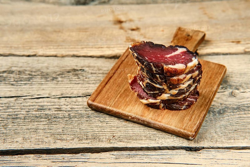 Close up view of smoked dried stacked slices of beef meat on wooden cutting board