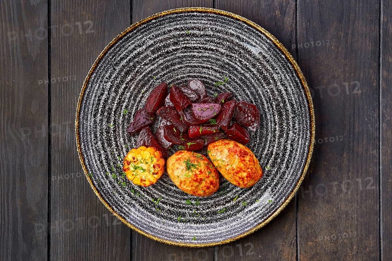 Top view of plate with fried pork cutlet with roasted beetroot slices and grilled maize on dark wooden table