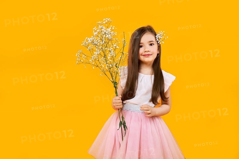 Cute young girl with wildflowers bouquet in hands on yellow background