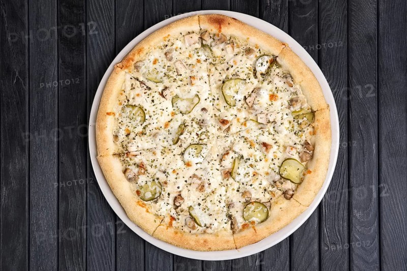 Top view of pizza with ham and slices of pickled cucumber