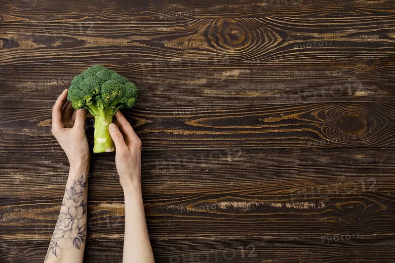 Overhead view of fresh broccoli in hands over wooden background
