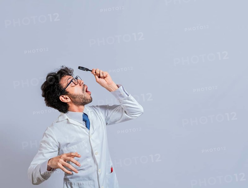 Surprised man in lab coat with magnifying glass looking at an advertisement above. Scientist man looking up with a magnifying glass. Amazed man observing an advertisement with a magnifying glass
