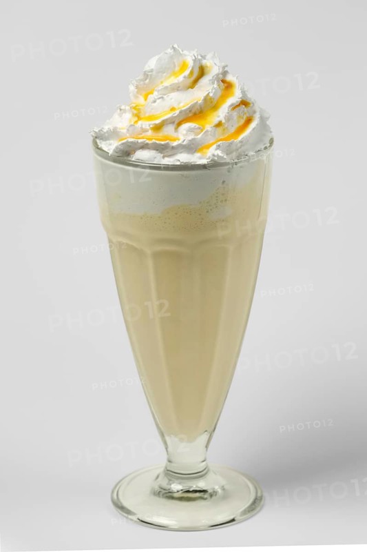 Mango and lemon milkshake summer cocktail in tall facetted glass on gray background