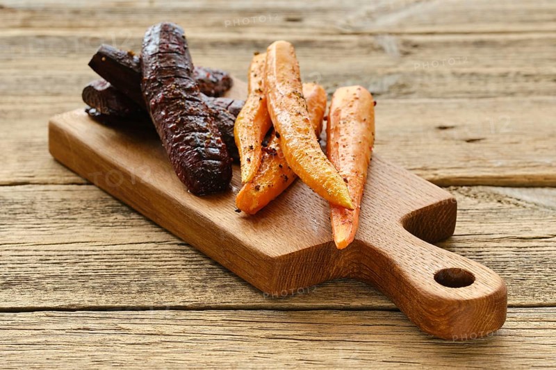 Baked carrot and beetroot with salt and pepper on wooden board