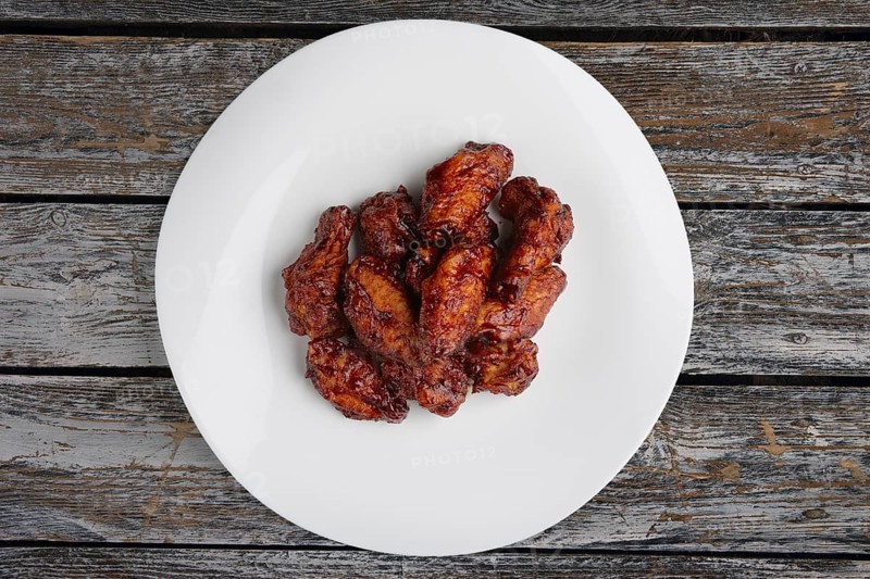 Tasty grilled chicken wings Buffalo on a white dish on wooden table