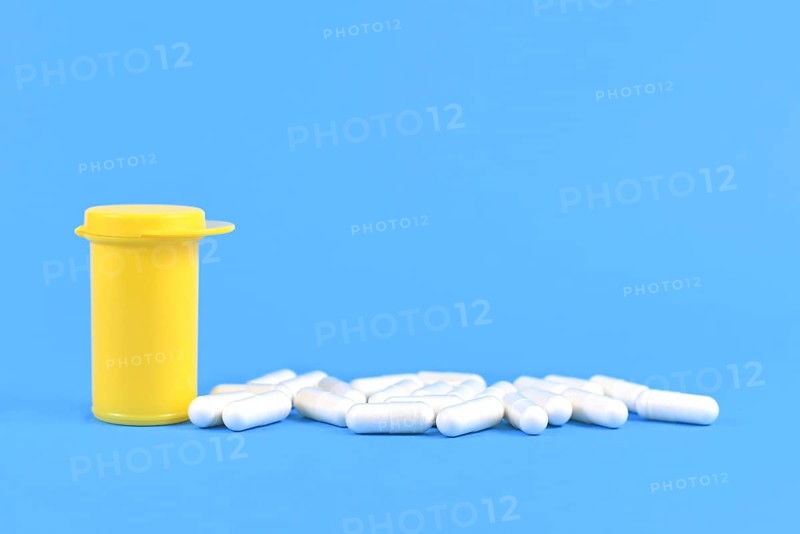 Capsule pills next to yellow medicine container on bright blue background