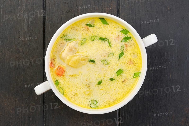 Overhead view of a bowl with hake soup with cream and carrot on a table