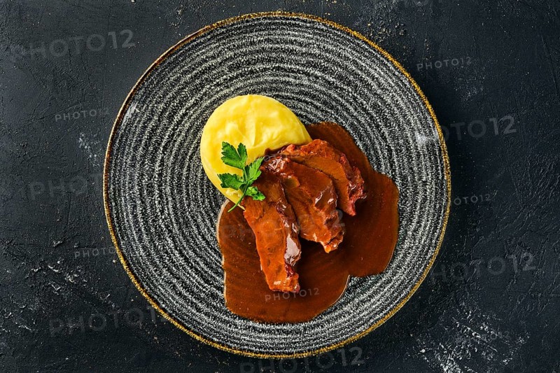 Overhead view of roasted beef slices with wine sauce and mashed potato on dark background