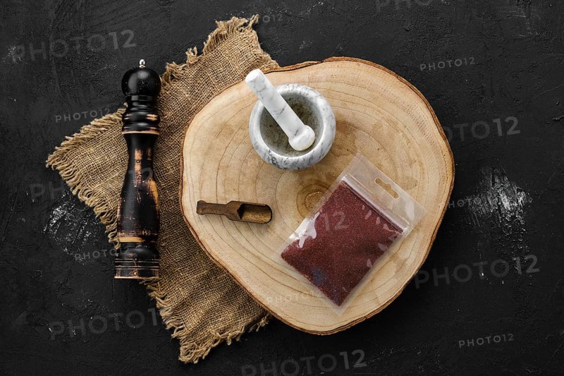 Wooden cross section with sumac in plastic package and stone mortar and mill