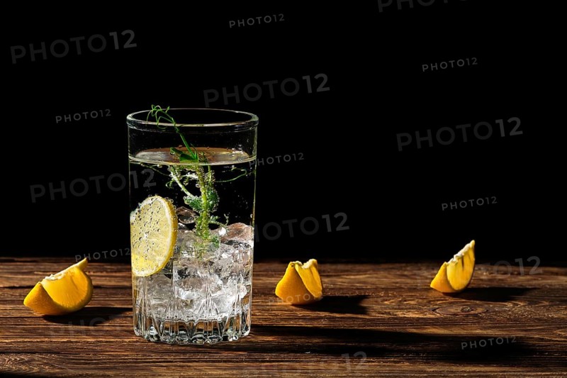 Carbonated cold water with ice and lemon casting a shadow on wooden table