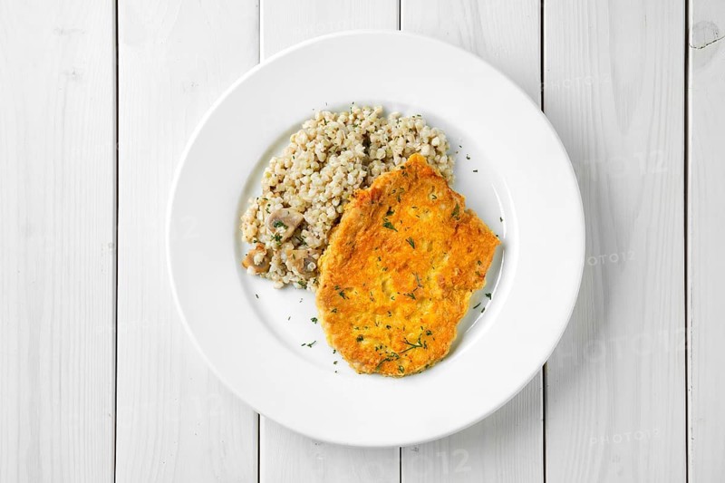 Top view of schnitzel with green buckwheat on white wooden table