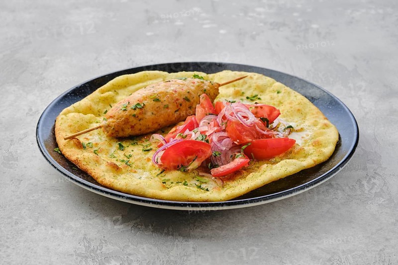 Kebab served on tortilla with tomato and red onion