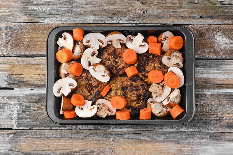 Lamb neck with champignon and vegetables baked in oven on wooden table