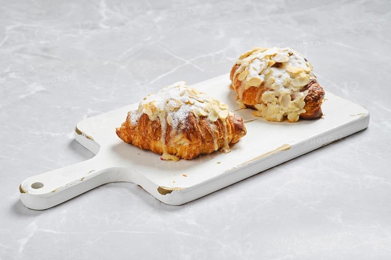 Crispy croissant with caramel and peanut shavings on white serving board on marble surface
